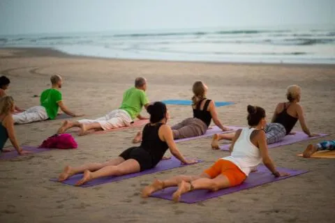 Group practicing cobra pose on mats along the beach