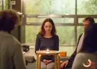 A group of people meditating with a lit candle in a dimly lit room.