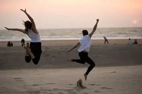 Two people jumping on a beach at sunset