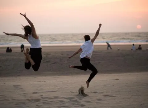Two women joyfully jumping on a beach during a yoga retreat at sunset