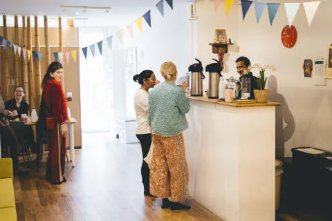 Students gathering and chatting around the reception tea counter in a yoga studio.