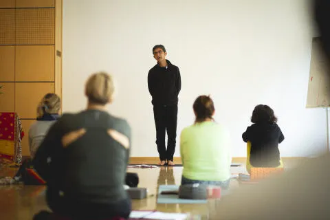 A male yoga instructor standing at the front of a class teaching students.
